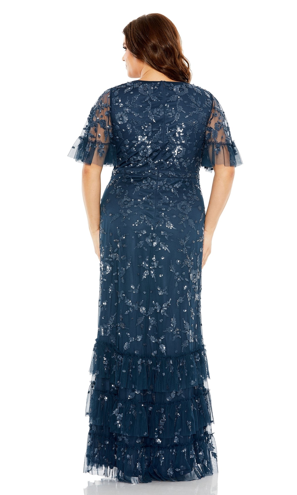 A woman is shown from the back wearing the Long Plus-Size Formal Dress 9270 by Mac Duggal—a navy blue, floor-length a-line gown with short sleeves, sequin floral patterns, and tiered ruffles.